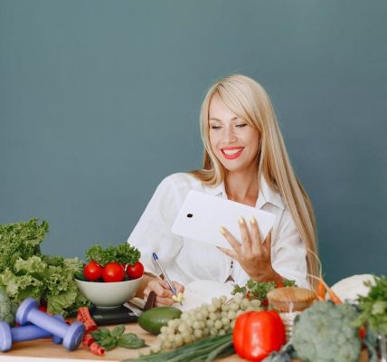 Woman using a tablet surrounded by fresh vegetables at a table, showcasing healthy lifestyle and technology.